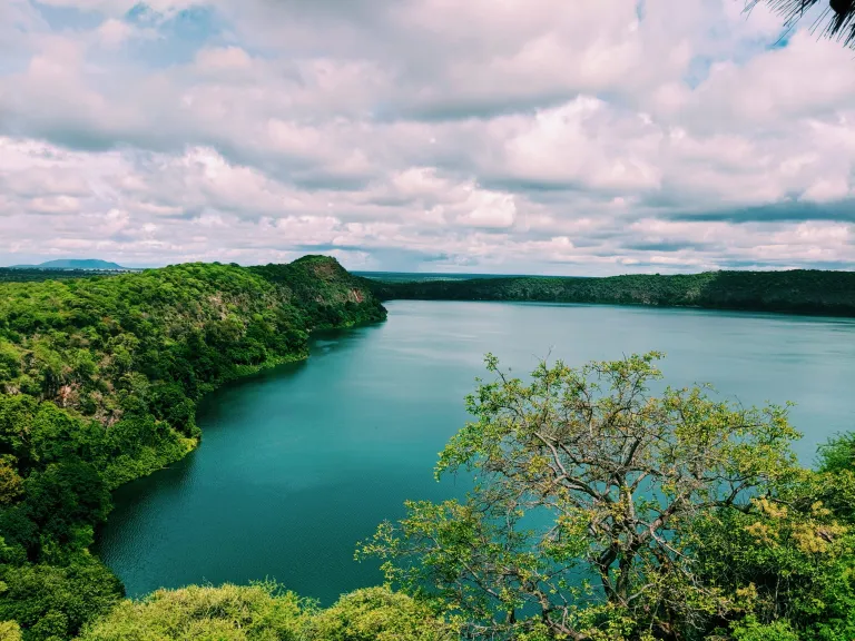 The deep emerald-blue crater lake of Chala on the Kenya-Tanzania border, surrounded by steep volcanic caldera walls and lush vegetation.