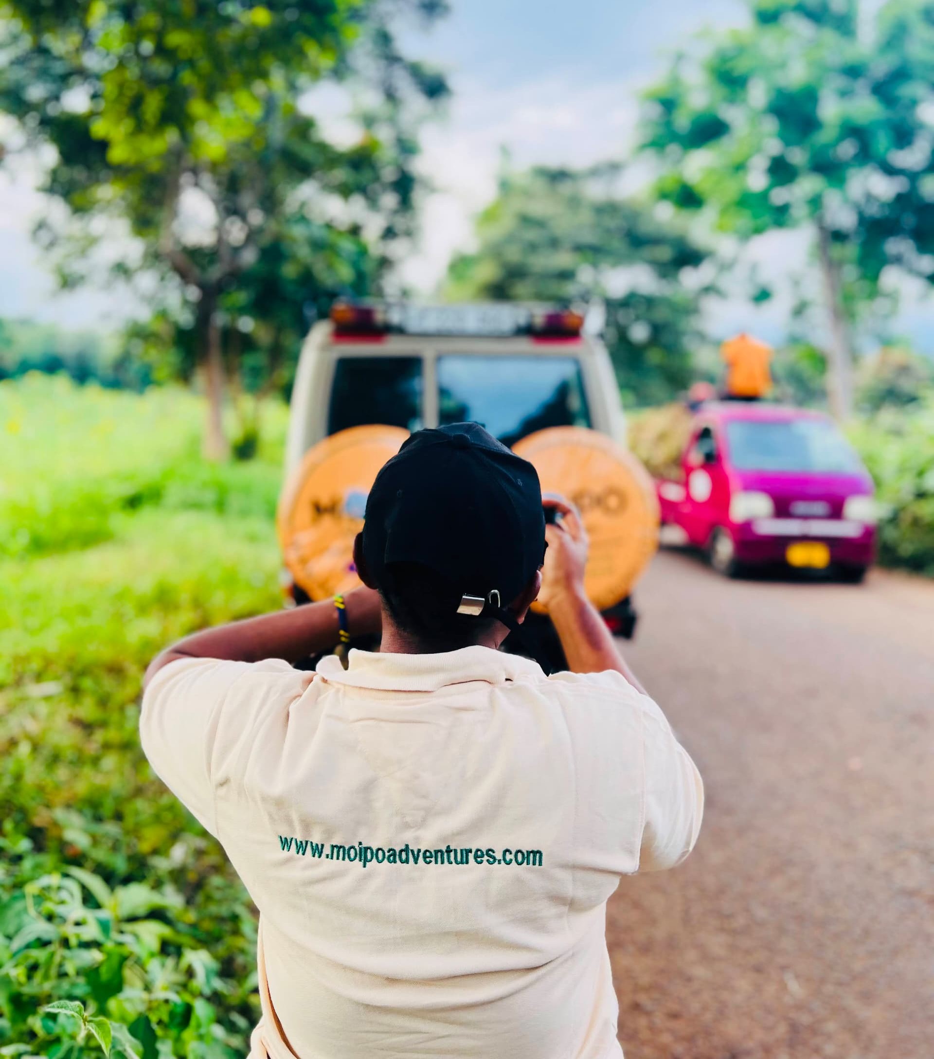 Rear view of a staff member wearing a Moipo t-shirt displaying the website link, standing next to a safari cruiser wrapped in Moipo branding and logos.
