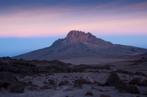 The jagged, rocky volcanic spires of Mawenzi Peak rising sharply above the clouds, captured from the high-altitude vantage point of Barafu Camp.