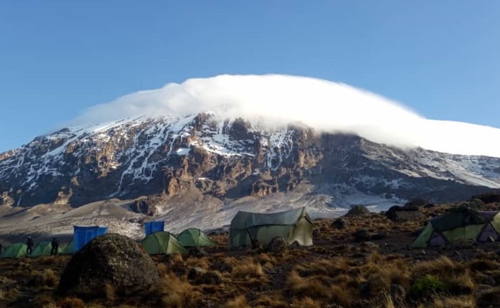 A striking view of Mount Kilimanjaro's upper slopes, featuring patches of pristine white snow partially veiled by dense, bright white summit clouds.